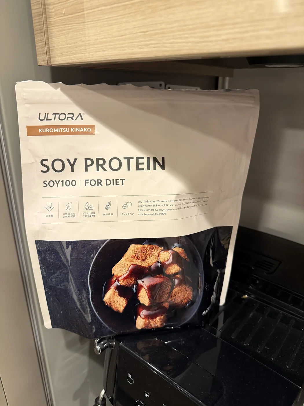 ULTORAのリニューアル版ソイプロテイン黒蜜きなこ風味810gのパッケージを自宅キッチンで自然光のもと撮影した写真